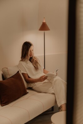 Pau Suites. Chica leyendo en el sofá de la habitación. Proyecto de interiorismo y decoración de Blanco Pimienta 